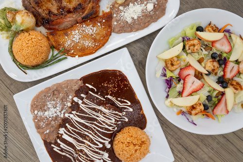 Hearty feast of Mexican food on the table family style consisting of mole enchiladas, carne asada steak, and shrimp fruit salad