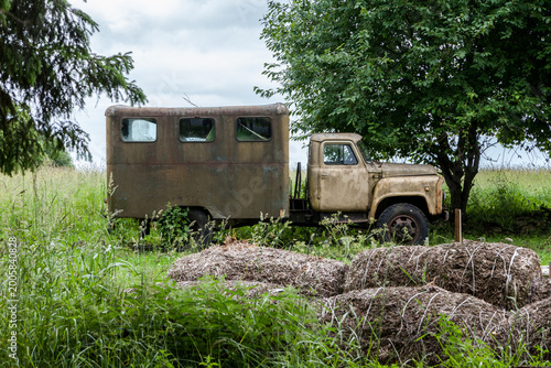 Billede på lærred Rusting Soviet-era GAZ-53 truck abandoned in tall grass beneath trees in Saarema