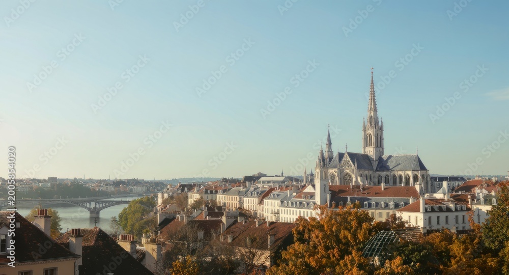 Obraz premium Picturesque cityscape with grand cathedral, river, bridge, and autumn foliage under blue sky