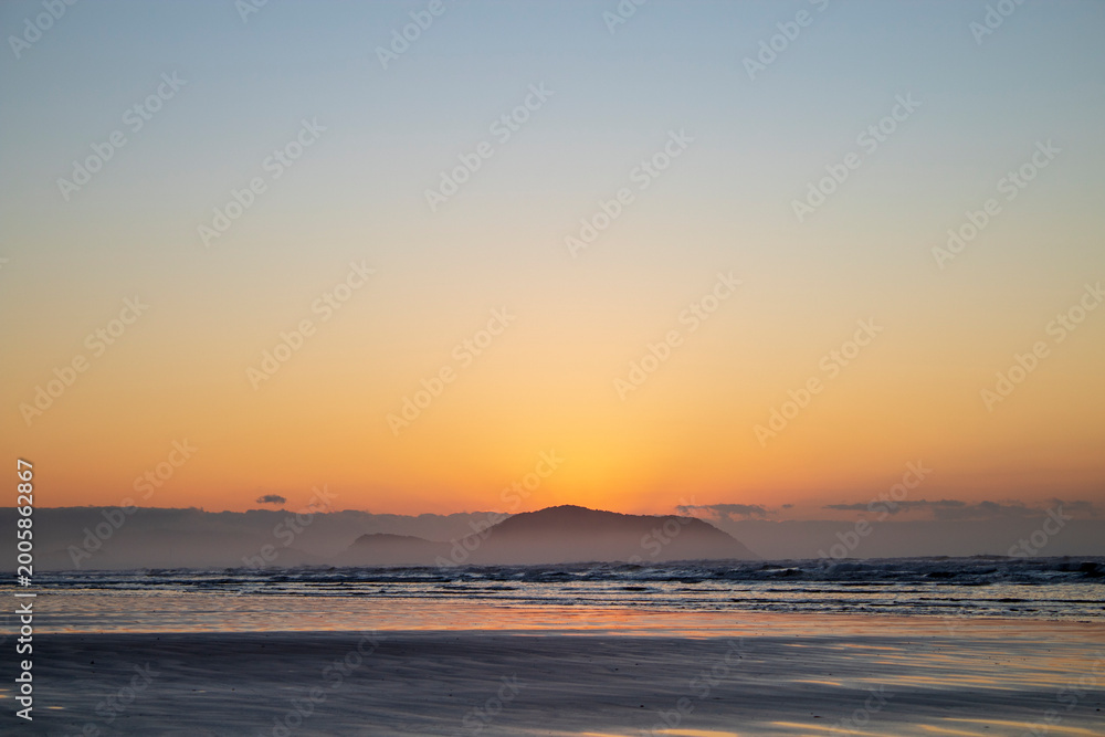 Fototapeta premium Golden Sunrise Over Ocean with Mountain Silhouette