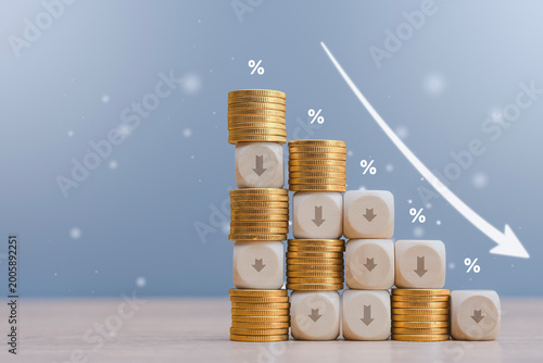 Foto Wooden blocks with down arrows and golden coins arranged in a declining graph pattern against a blue background