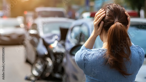 Woman reacts with visible shock and panic while clutching her head at the scene of a recent traffic accident involving two damaged vehicles.
