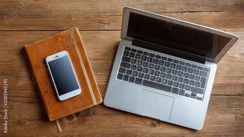 Modern workspace featuring a smartphone, open laptop, and leather notebook on a rustic wooden table for productivity and creativity branding