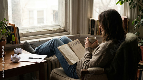 A woman thinking about 2027 goals while reading book at home, planning future ideas, personal growth, reflection, a cosy lifestyle, mindset, self-improvement concepts.