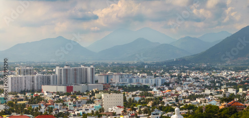 Canvastavla A panoramic view of the city of Nha Trang, Vietnam, with modern high-rise buildings and traditional houses nestled against a backdrop of misty mountains