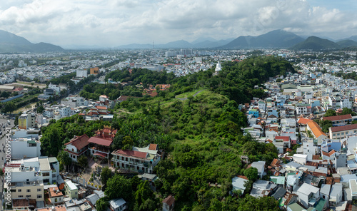 Nha Trang, Vietnam - An aerial view captures the sprawling cityscape with lush green hills and a prominent white Buddha statue at Long Son Pagodaoverlooking the urban landscape.