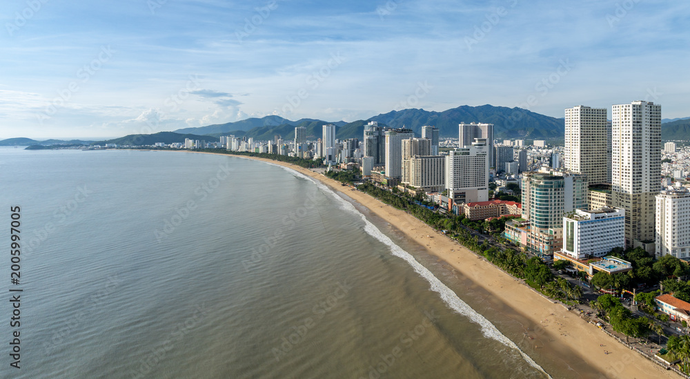 Obraz premium Aerial view of Nha Trang beach, Vietnam. The city's coastline is lined with hotels and palm trees, with mountains in the background.