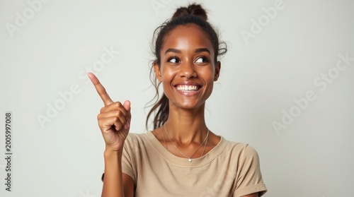 Young black woman with her hair in a bun smiles widely and points upwards and to the side with her index finger looking curious young adult
