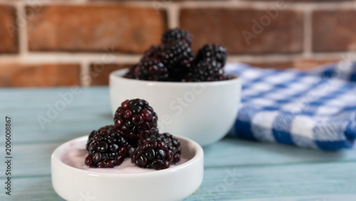 Quadro su tela Blackberries rest in white bowls on a rustic blue surface