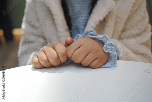 Vászonkép Child sits at table with hands clasped in waiting posture