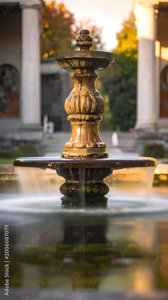 Naklejka premium A serene fountain in a park with columns and greenery