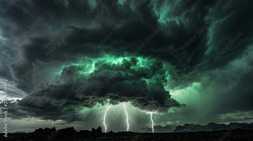 Fototapeta premium Intense lightning bolts strike from massive dark green storm clouds looming over a jagged rocky landscape during a powerful night thunderstorm that illuminates the entire horizon with electric energy.