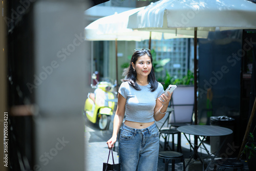 Young woman holding a smartphone and walking with shopping in urban city