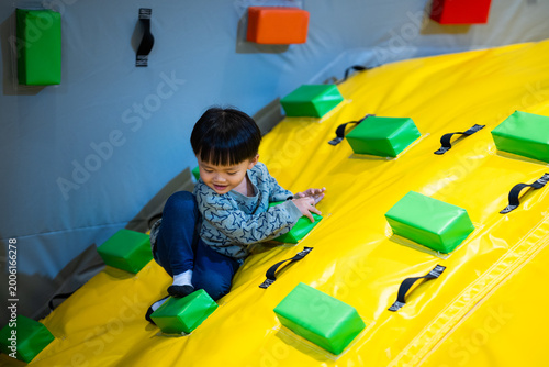 Asian boy climbing colorful inflatable slide at indoor playground, active childhood lifestyle, physical development, playful authentic moment, tactile sensory experience, vibrant indoor activity