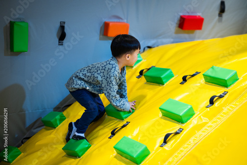 Asian boy climbing colorful inflatable slide at indoor playground, active childhood lifestyle, physical development, playful authentic moment, tactile sensory experience, vibrant indoor activity