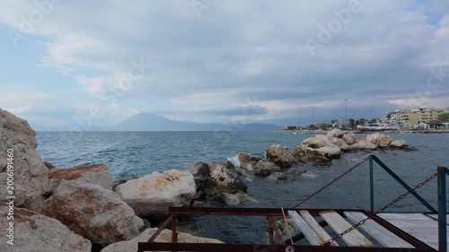 Rusted ladder platform on rocky breakwater facing open sea and mountains