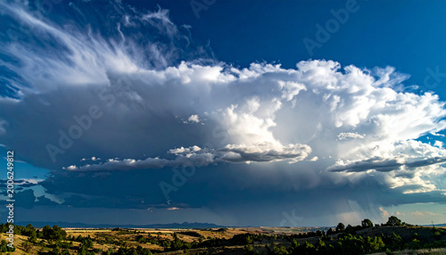 Enso cloud formation over rolling grassland and distant hills with dramatic climate storm towering across blue sky bringing light and shadow to states landscape