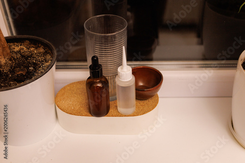 Three containers with oils and a glass rest on a shelf beside house plants in a home at night