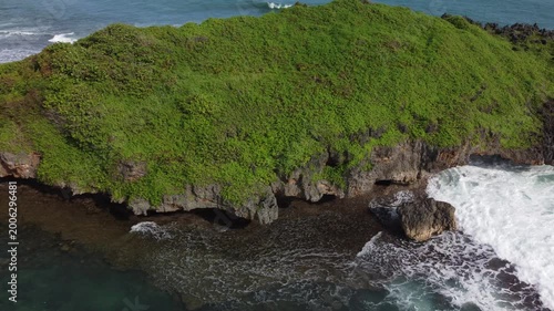 Aerial view of a stunning coral island from the beach with steep cliffs, turquoise water and dynamic ocean waves.