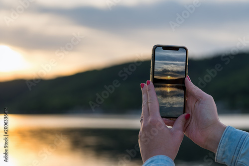 Person photographing sunset over lake with smartphone