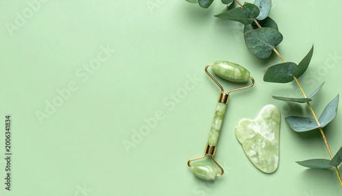 Jade roller and gua sha facial tools with eucalyptus leaves on a pastel green background.