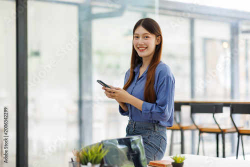 Obraz na plátne Smiling woman using smartphone in modern office