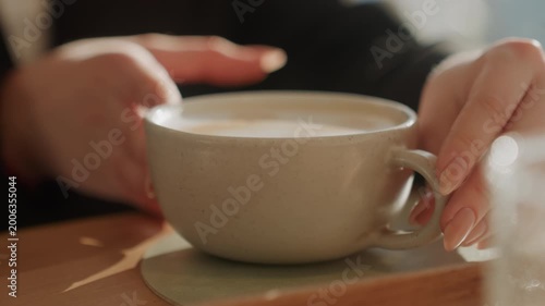 Warm cafe hands holding latte cup, soft sunlight and foam detail capture calm ritual of patron cradling ceramic mug on wooden table, slow deliberate gestures, creamy crema, subtle steam, natural light