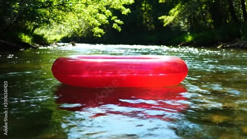Red inflatable ring floating peacefully in a flowing river on a sunny day with lush green foliage