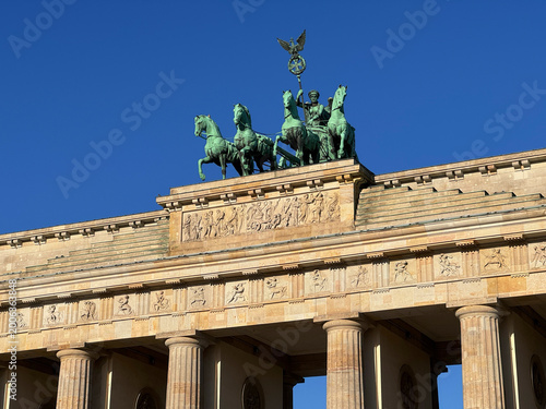Brandenburg Gate with its iconic bronze quadriga and goddess Victoria against a clear blue sky in central Berlin.