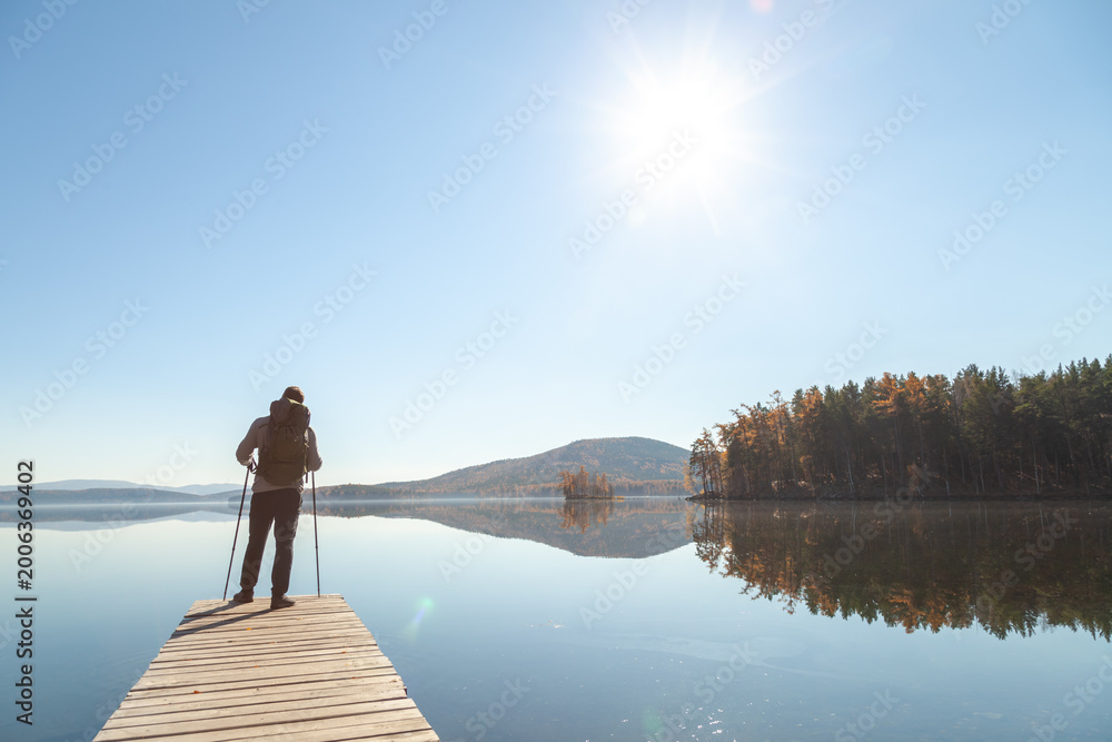 Naklejka premium A man admires the landscape of a mountain lake while standing on the pier