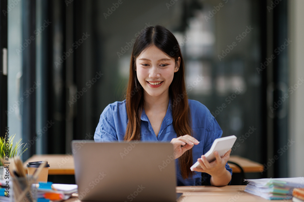 Fototapeta premium Asian business woman smiling calculating finances in office