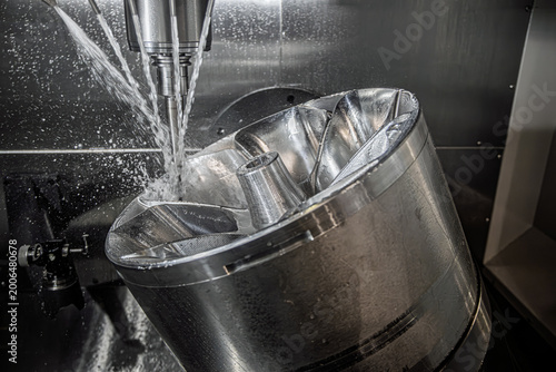 Foto CNC milling machine machining metal impeller with coolant spray.