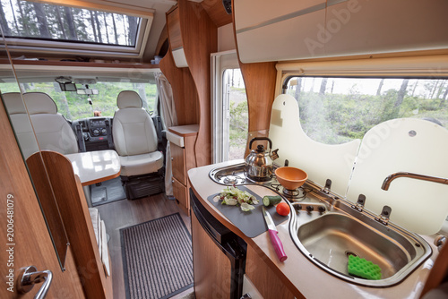 Modern motorhome interior with kitchen and dining area in forest campsite.