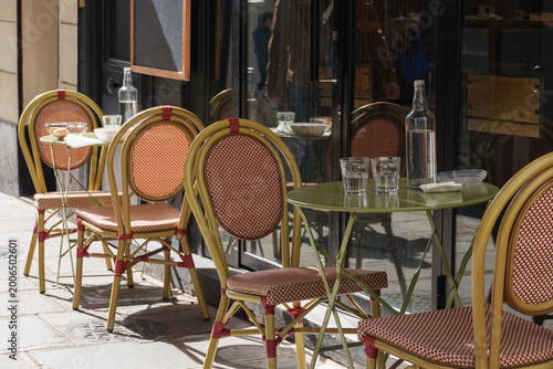 Photography Empty Paris cafe table with woven chairs and glassware on quiet street corner in