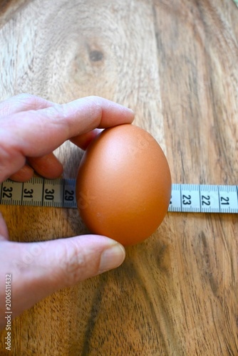 Hand holding brown egg with measuring tape representing egg dieting, weight loss and healthy eating concepts. Minimal composition with Copy Space.