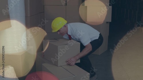 Worker stacking boxes in warehouse, bending to lift box and causing back pain under bokeh overlays