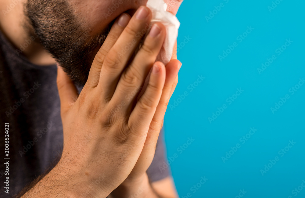 Fototapeta premium Close-up of a man using a tissue, capturing cold, sickness, or allergy symptoms against blue.