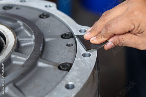 ​Technician hands manually sanding and cleaning the metal surface of a transmission housing to ensure a smooth seal during a gearbox rebuild.
