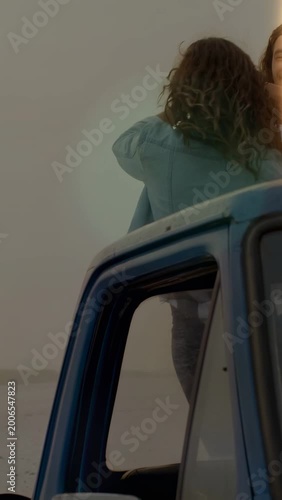Vertical video: Couple climbing blue pickup cab for travel content, forming heart, holding bottle