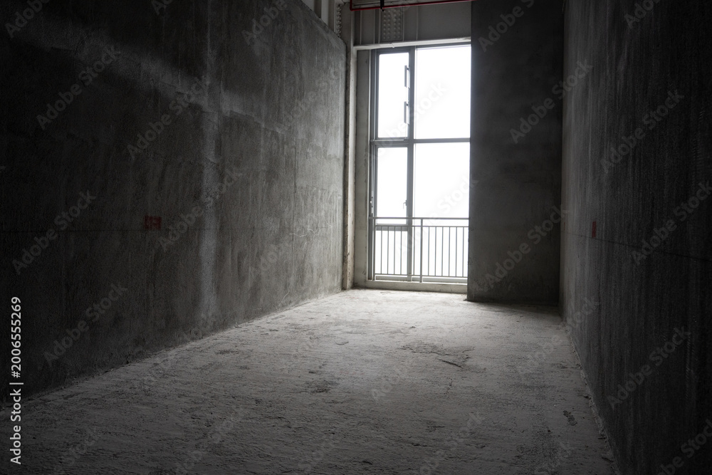 Fototapeta premium Bare concrete corridor in an unfinished apartment with large window allowing natural light to enter