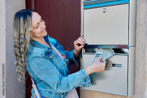 Bild auf Leinwand Smiling woman putting US dollar bills into a silver metal mailbox