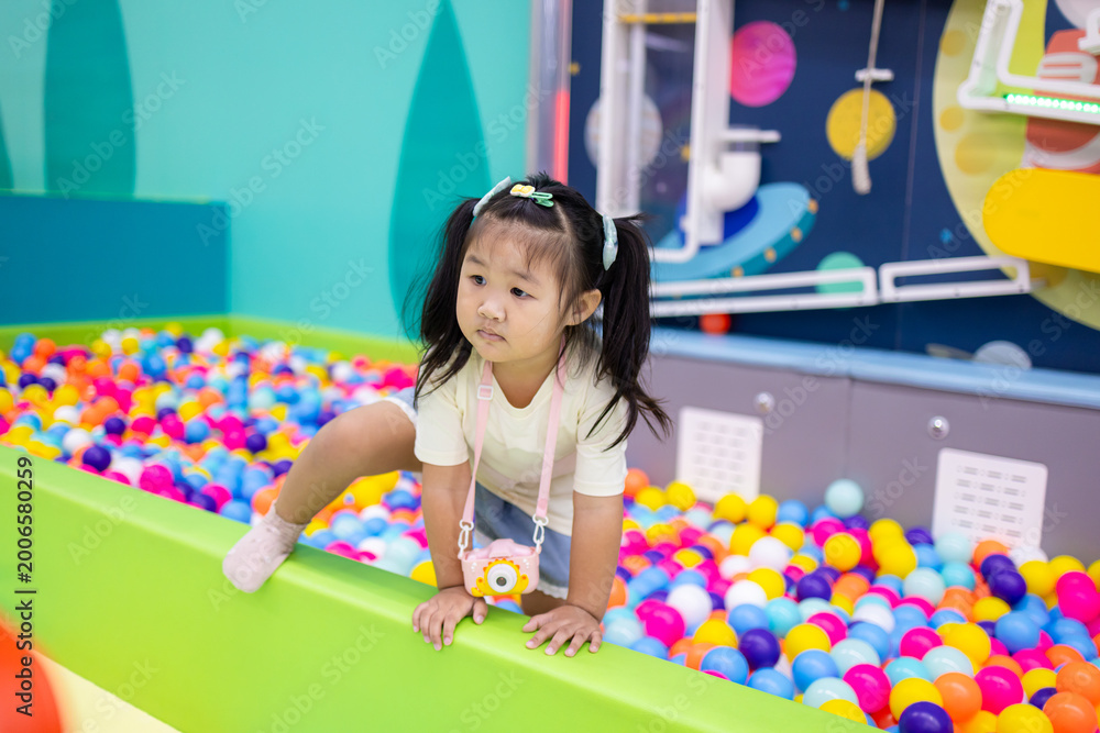 Fototapeta premium Little Asian girl playing with interactive ball wall at indoor playground,An adorable young Asian girl is focused on playing with an interactive ball physics game and a colorful ball pit at a modern.