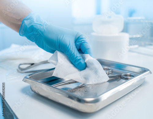 Hand using a sanitizing wipe to clean a medical instrument in a sterile environment for patient safety.