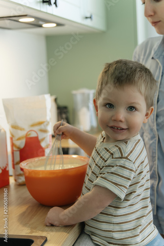 Happy toddler cooking in kitchen, child mixing ingredients in bowl, family lifestyle and early learning at home