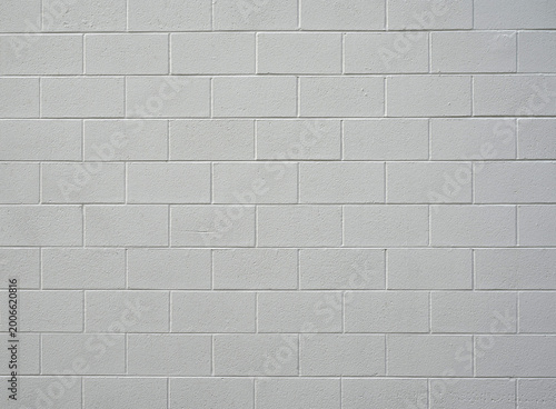 Close up of painted white cinder block wall with rough coarse concrete blocks, smooth mortar grooves, long gouge in one block, and soft natural lighting