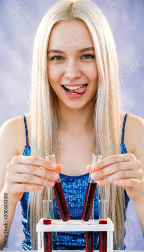 A playful platinum-blonde woman in a sequined blue top sticks her tongue out while holding red test tubes against a lavender backdrop. Generative AI