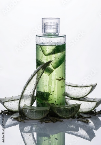Minimalistic composition with aloe vera shampoo, fresh leaves, and water droplets on a bright background