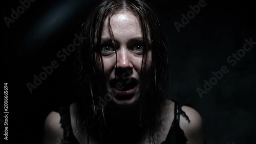 Terrified woman screams with fear in a dark, claustrophobic environment; horror scene