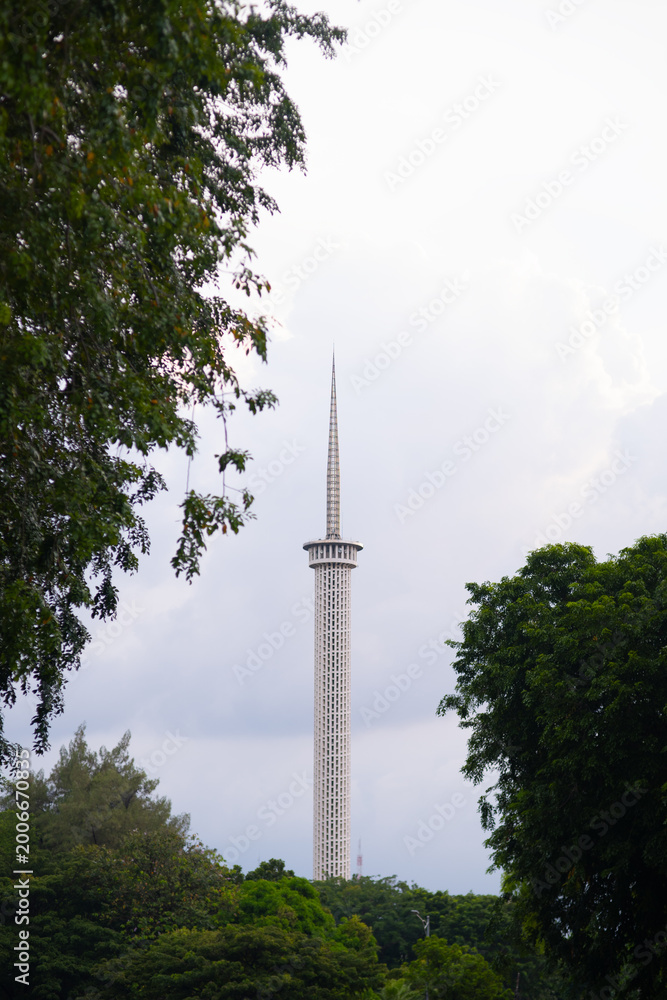 Obraz premium The tall, iconic minaret of Istiqlal Mosque in Jakarta seen through lush green trees under a bright sky