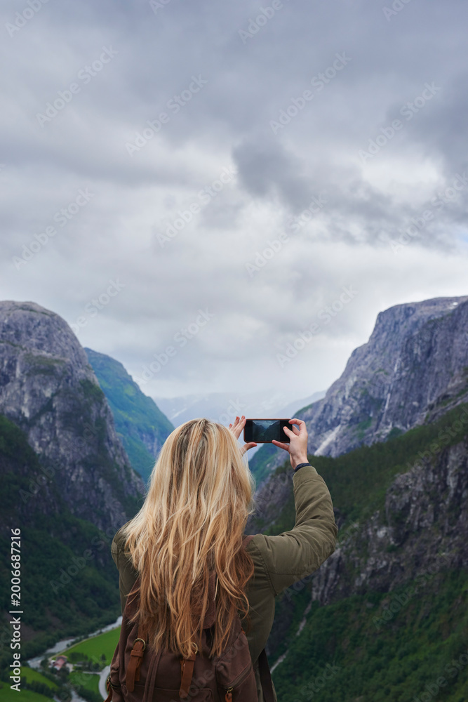 Fototapeta premium Woman, adventure or mountain with phone for picture of landscape, outdoor memory or photography. Back view, female person or tourist with smartphone for travel or capture moment of natural scenery